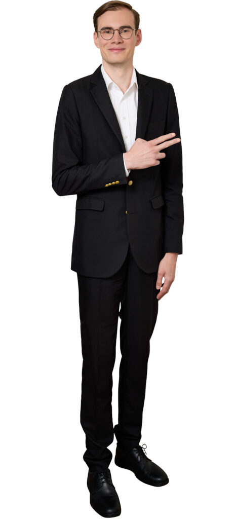 Man in a black suit and white shirt, wearing round glasses, smiling and making a peace sign with his right hand.