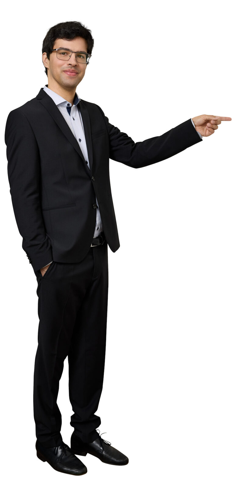 Man in a black suit and glasses points to the right with his arm extended.