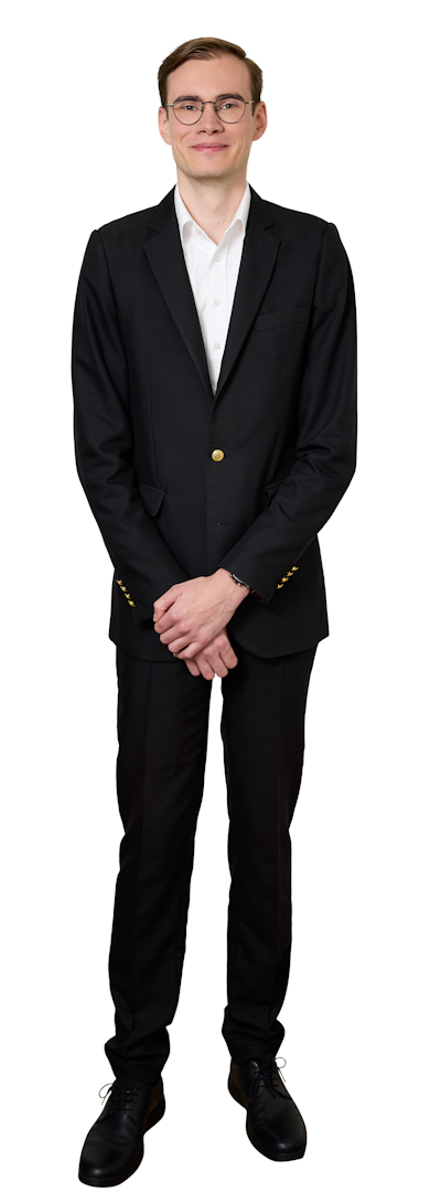 Man in a black suit and white shirt standing with hands clasped, looking at the camera.